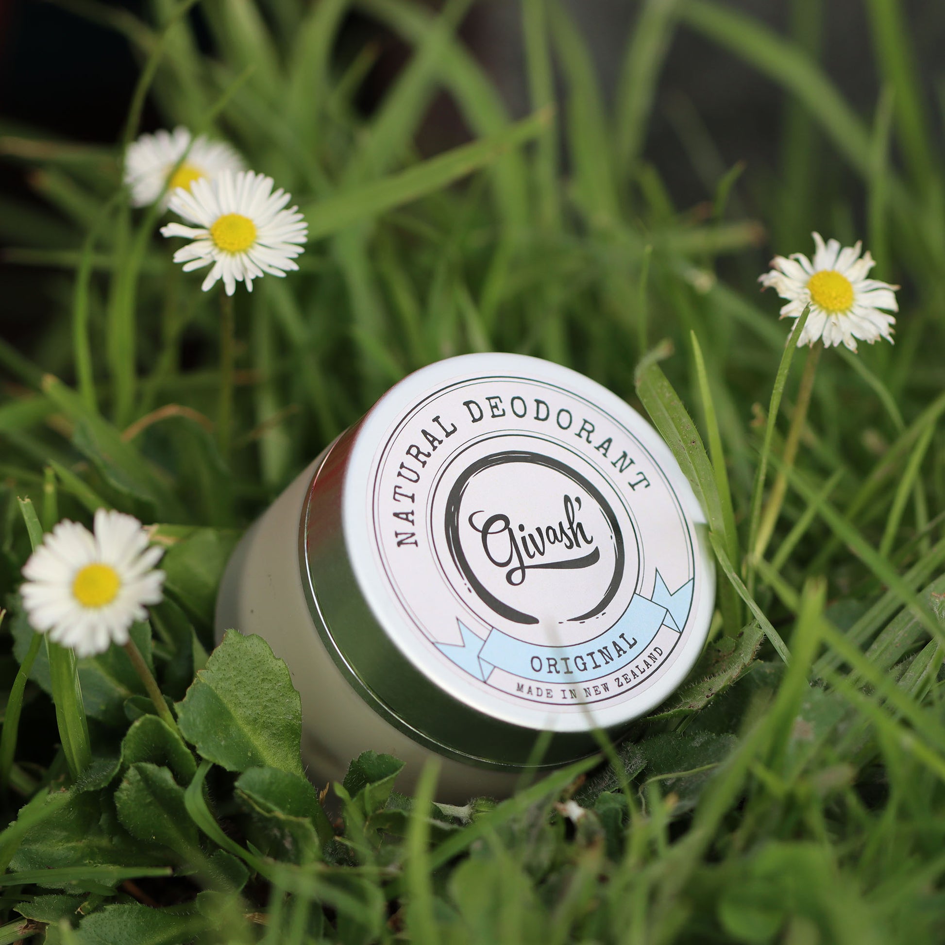 Givash natural deodorant in a jar picture taken sitting in fresh green grass with daisies around it.
